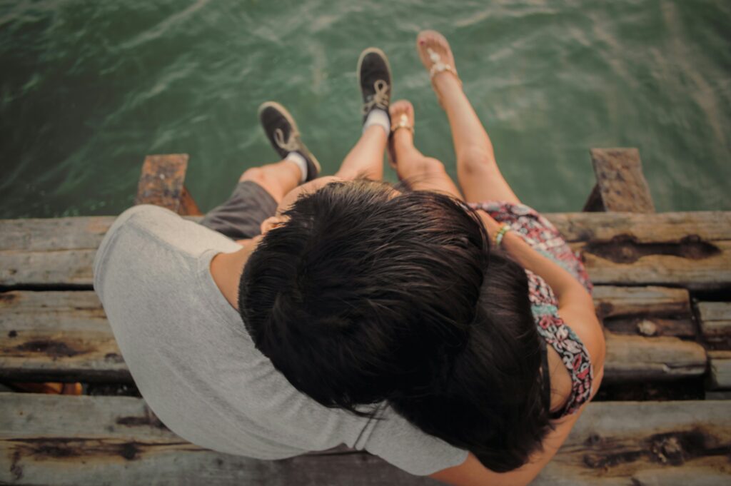 photo from above of a man and woman sitting on a dock embracing with a strengthened relationship