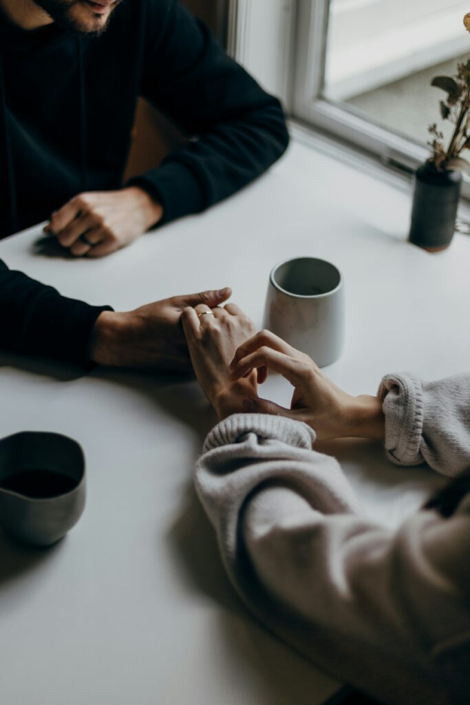 A couple's hands holding across a coffee table during online relationship counseling